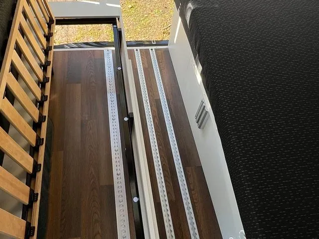 Blick von oben auf den Holzboden mit drei Schienen, links der hochgeklappte Lattenrost, rechts die Sitzbank