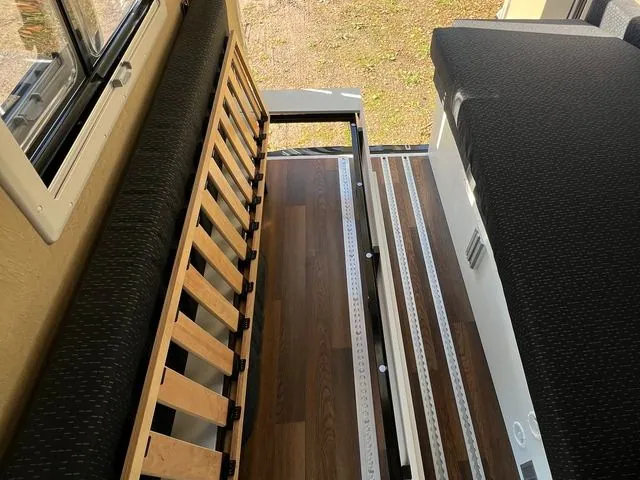 Hochgeklappter Lattenrost links, freier Holzboden mit Schienen, rechts die Sitzbank