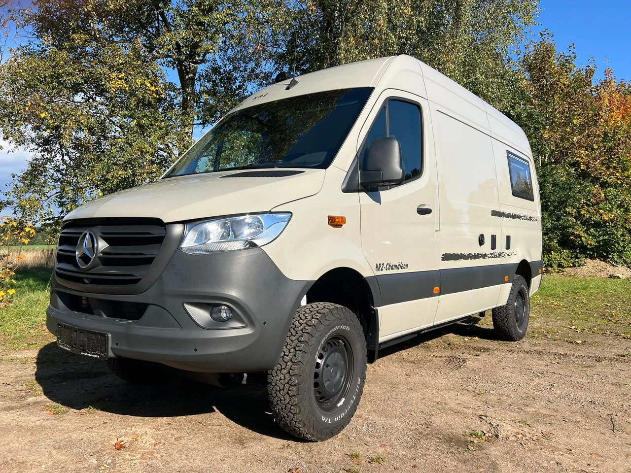 HRZ Chamäleon 4x4 von vorn links auf einem Feldweg im Herbst: Lack in Steingrau, anthrazitfarbene Stoßfänger, All-Terrain-Reifen auf schwarzen Stahlfelgen
